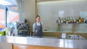 A bar area with a counter, shelves of liquor bottles, and a person standing behind the counter. - Falco (Riccione)