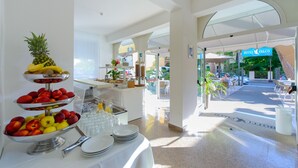 A buffet area with fruit and beverages, a reception desk, and outdoor seating. - Falco (Riccione)
