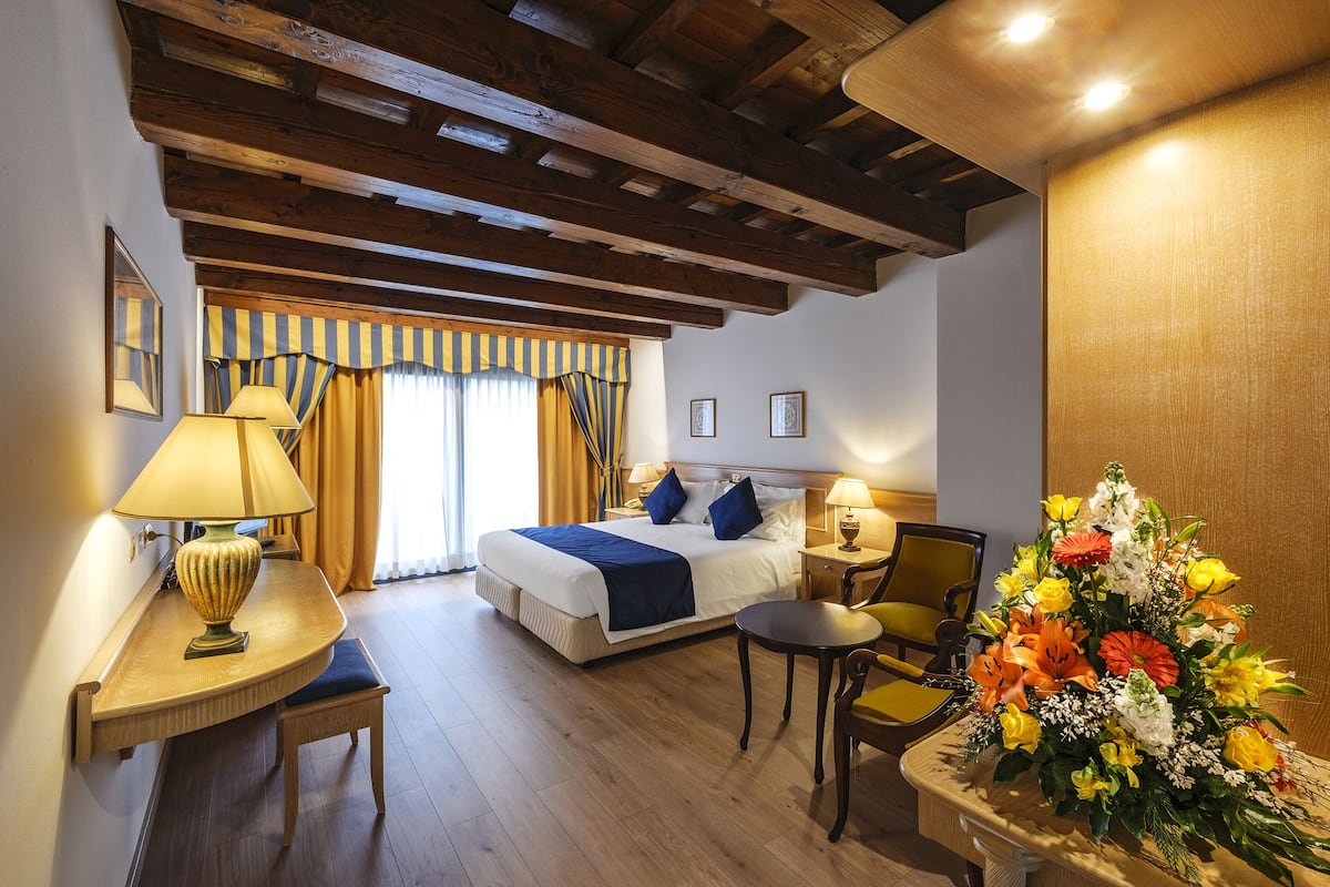 Una habitación de hotel con una cama, mesitas de noche, un escritorio, una silla y un gran arreglo floral.