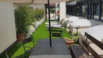A patio with a table and chairs, surrounded by a small garden and a white umbrella.