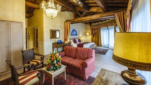 A hotel room with a wooden ceiling, a chandelier, a sofa, a table with flowers, and a bed with curtains. - Hotel Orologio (Ferrara)