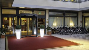 A hotel entrance with a red carpet, glass doors, and a row of bicycles parked outside. - Hotel Orologio (Ferrara)