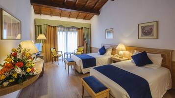 A hotel room with two beds, a desk, a chair, a table, and a floral arrangement.
