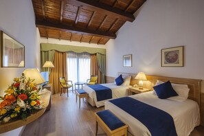 Habitación de hotel con dos camas, un escritorio, una silla, una mesa y un arreglo floral.