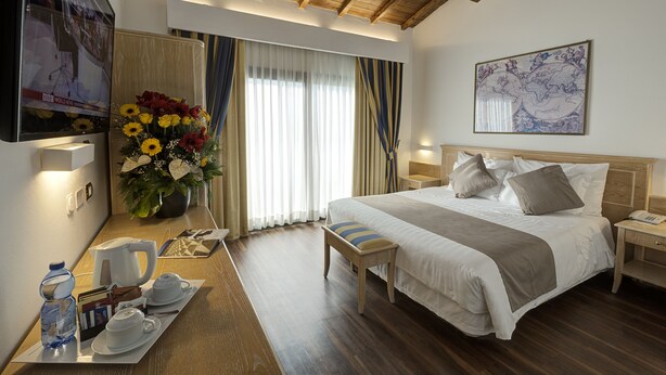 A hotel room with a large bed, a wooden ceiling, a TV on the wall, a flower arrangement, and a breakfast tray. - Hotel Orologio (Ferrara)
