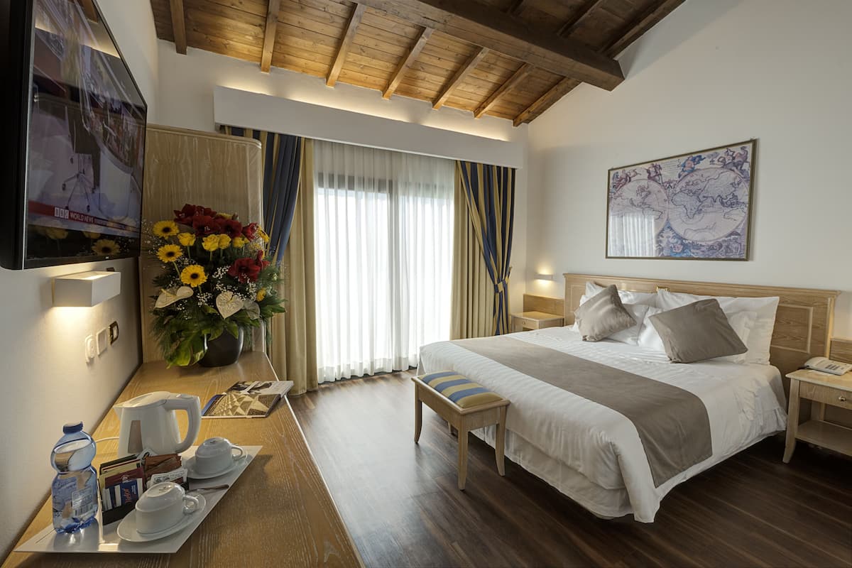 Habitación de hotel con una cama grande, techo de madera, televisor, una mesa de centro con alimentos para el desayuno y una ventana con cortinas.