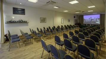 A conference room with rows of chairs, a projector screen, and a painting on the wall.