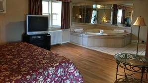 Habitació d'hotel amb llit, televisió, un gran mirall, banyera i taula de vidre.