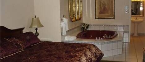 A hotel room with a large bed, a bathroom with a bathtub, and a painting on the wall.