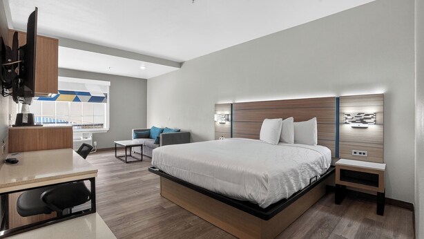 A modern hotel room with a large bed, a desk, a chair, a TV, and a view of the outside. - Sonesta Essential Hotel Houston-I-45 Spring (Houston)