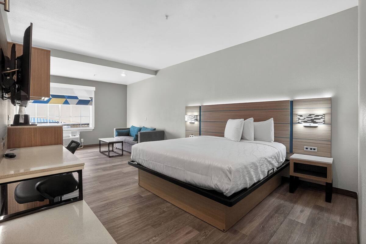 A modern hotel room with a large bed, a desk, a chair, a TV, and a view of the outside.
