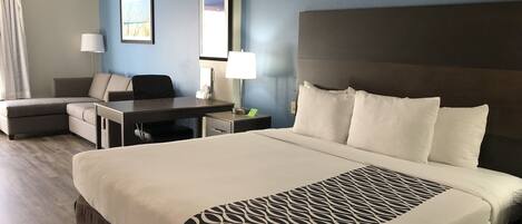 Een hotelkamer met een groot bed, een bureau, een stoel, een lamp en een schilderij aan de muur.