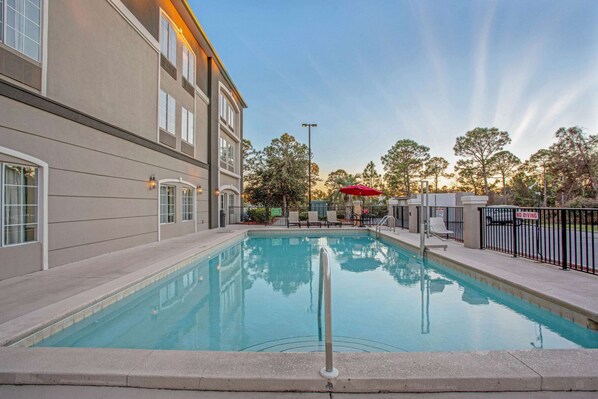 A swimming pool with a metal railing, surrounded by a building with large windows and a red umbrella. - La Quinta by Wyndham PCB Coastal Palms (Panama City Beach)