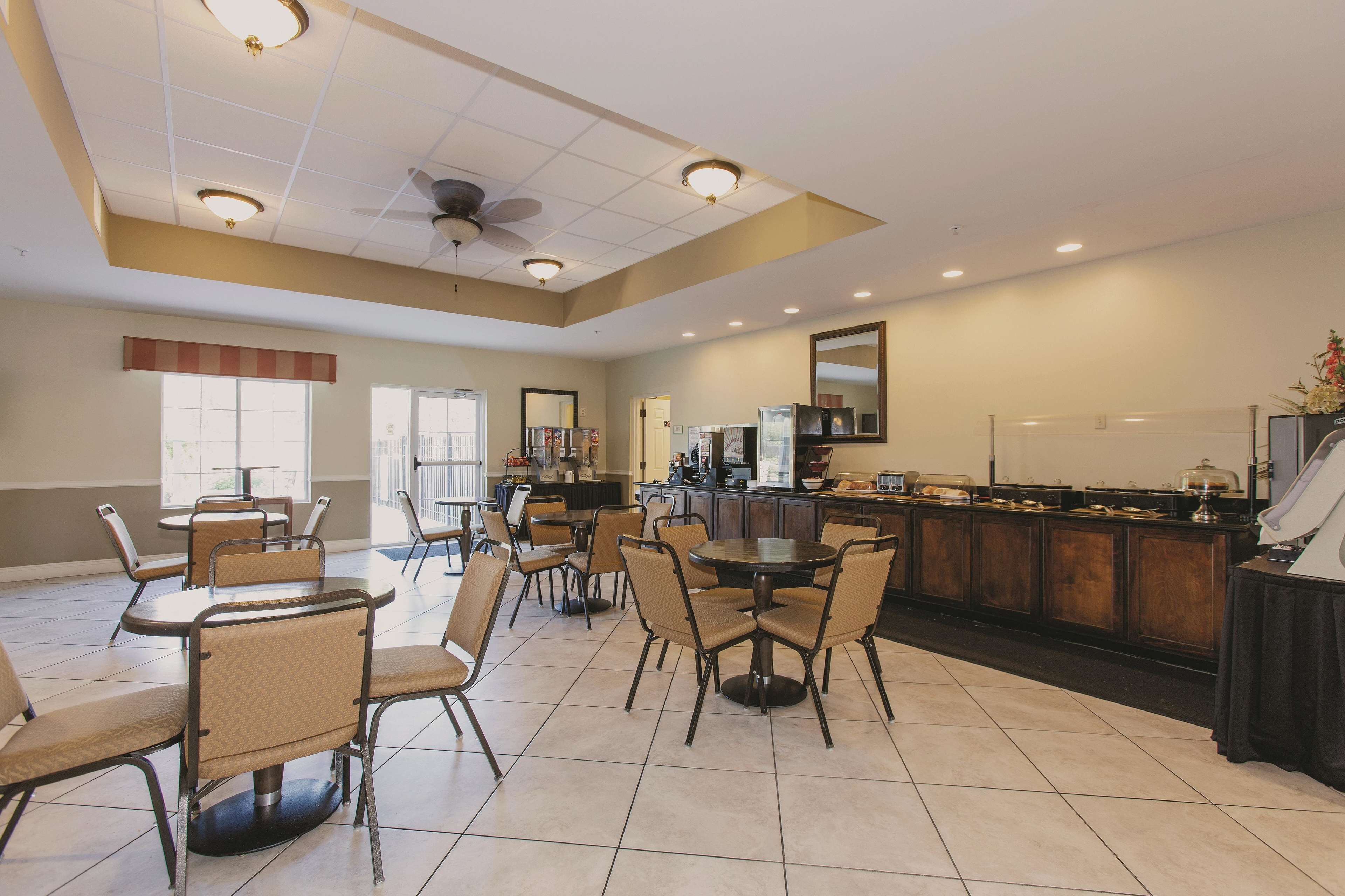 A spacious dining area with multiple tables and chairs, a kitchen counter with food display, and a ceiling fan.