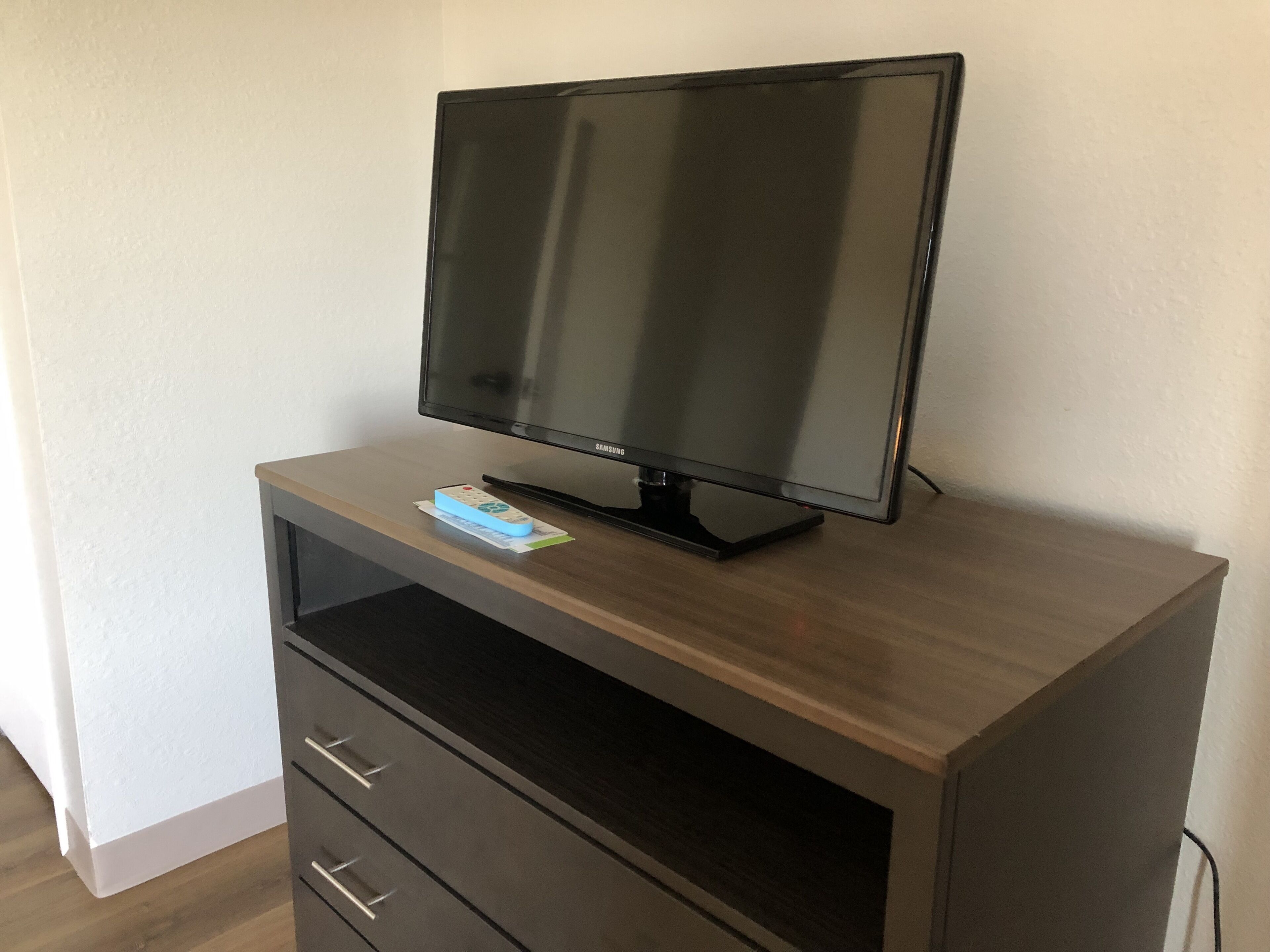 A Samsung TV on a wooden TV stand with a remote control.