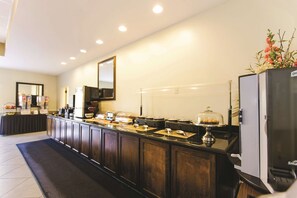 A hotel kitchen with a long counter, a refrigerator, and a buffet area. - La Quinta by Wyndham PCB Coastal Palms (Panama City Beach)