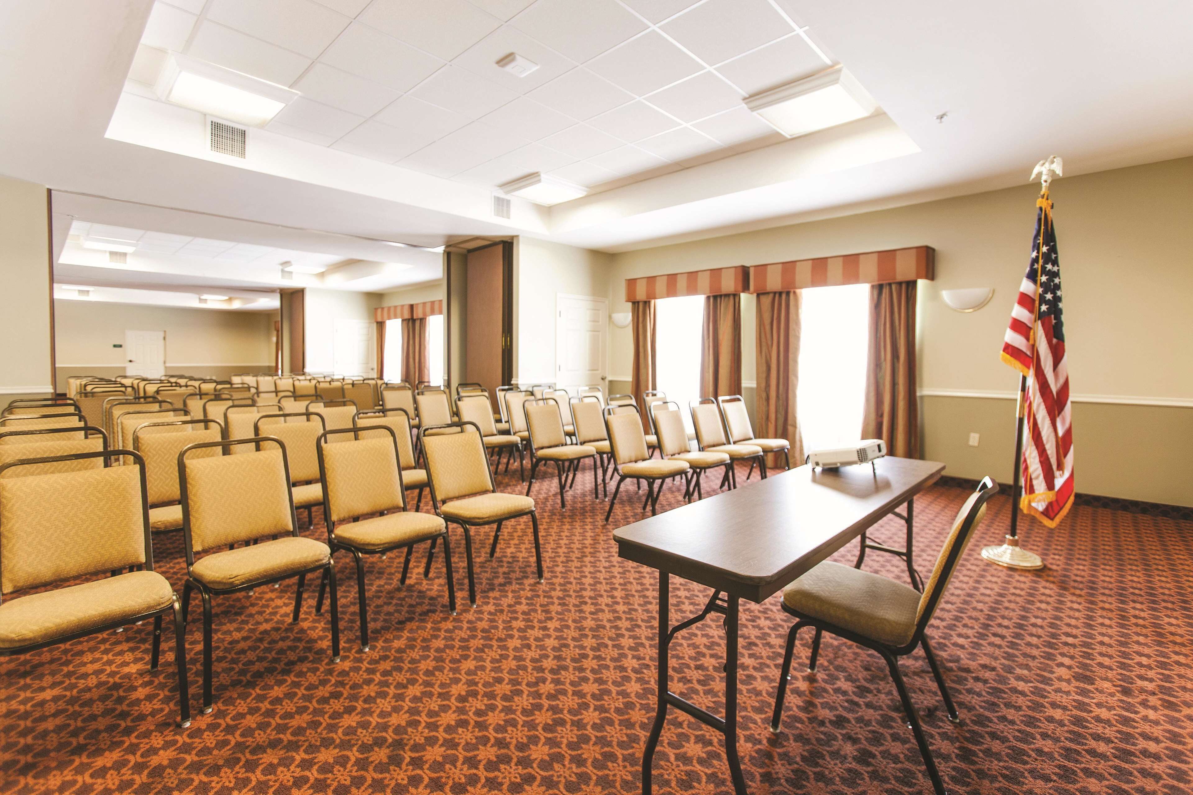 Une salle de conférence avec des rangées de chaises, une longue table et un drapeau américain.