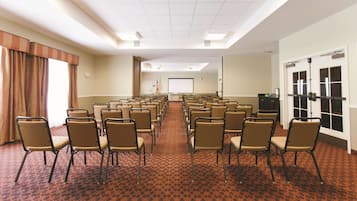 A conference room with rows of chairs, a carpeted floor, and a projector screen.