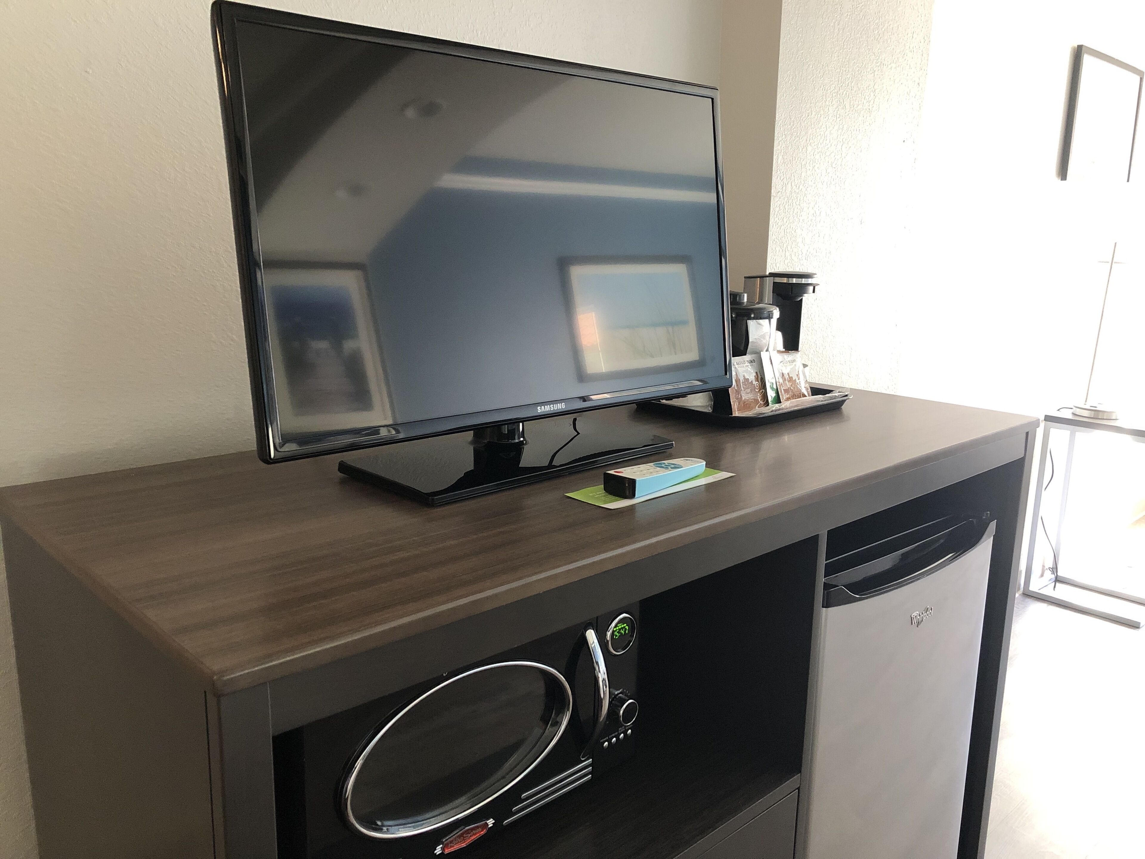 A Samsung TV on a wooden desk with a coffee machine and a remote control.