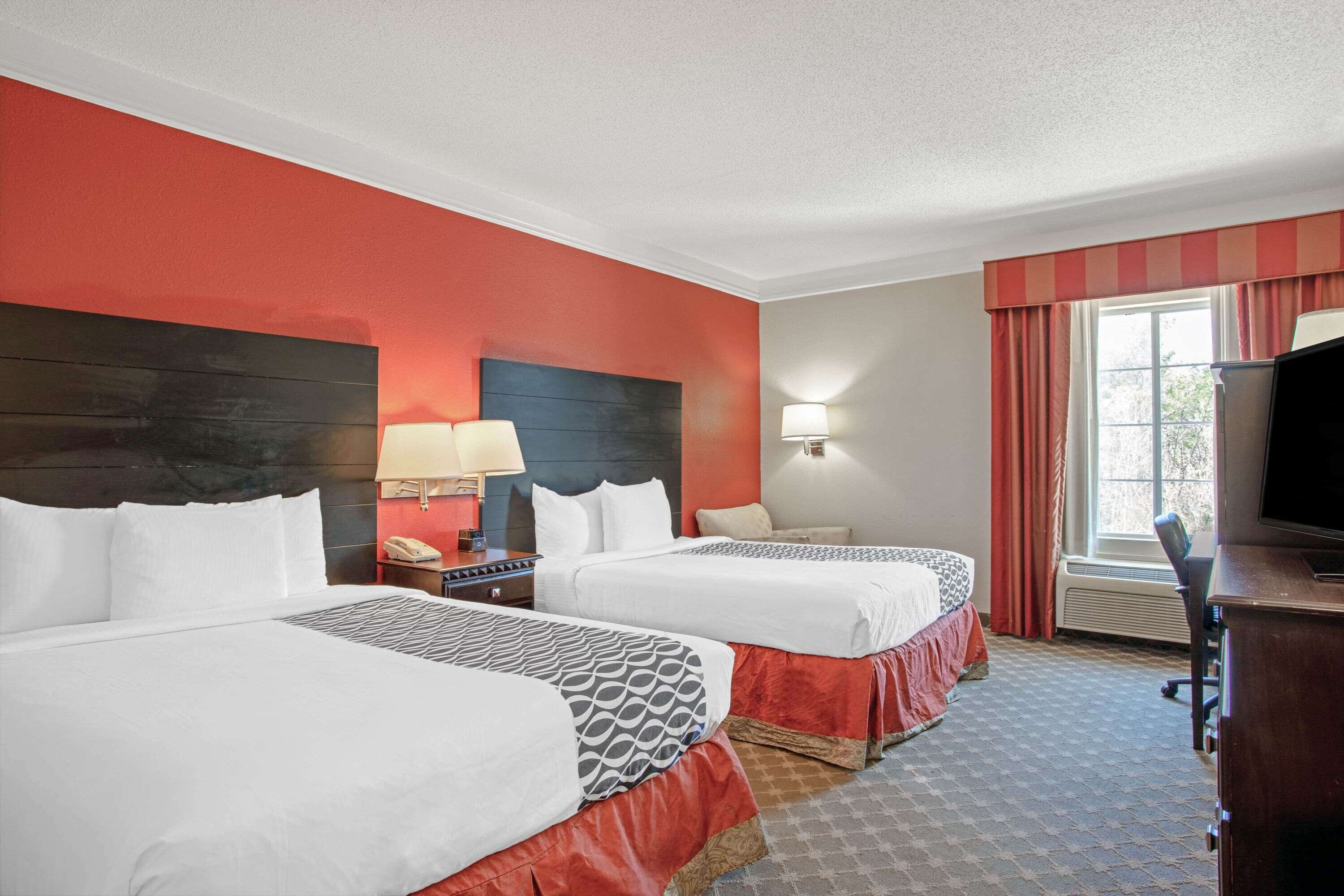 A hotel room with two beds, a desk, a TV, and a window with curtains.
