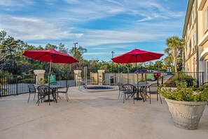 An outdoor patio with tables and chairs, two red umbrellas, a small pool, and a large planter. - La Quinta by Wyndham PCB Coastal Palms (Panama City Beach)