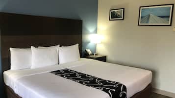 A hotel room with a large bed, white bedding, a black and white patterned throw, a nightstand with a lamp, and two framed pictures on the wall.