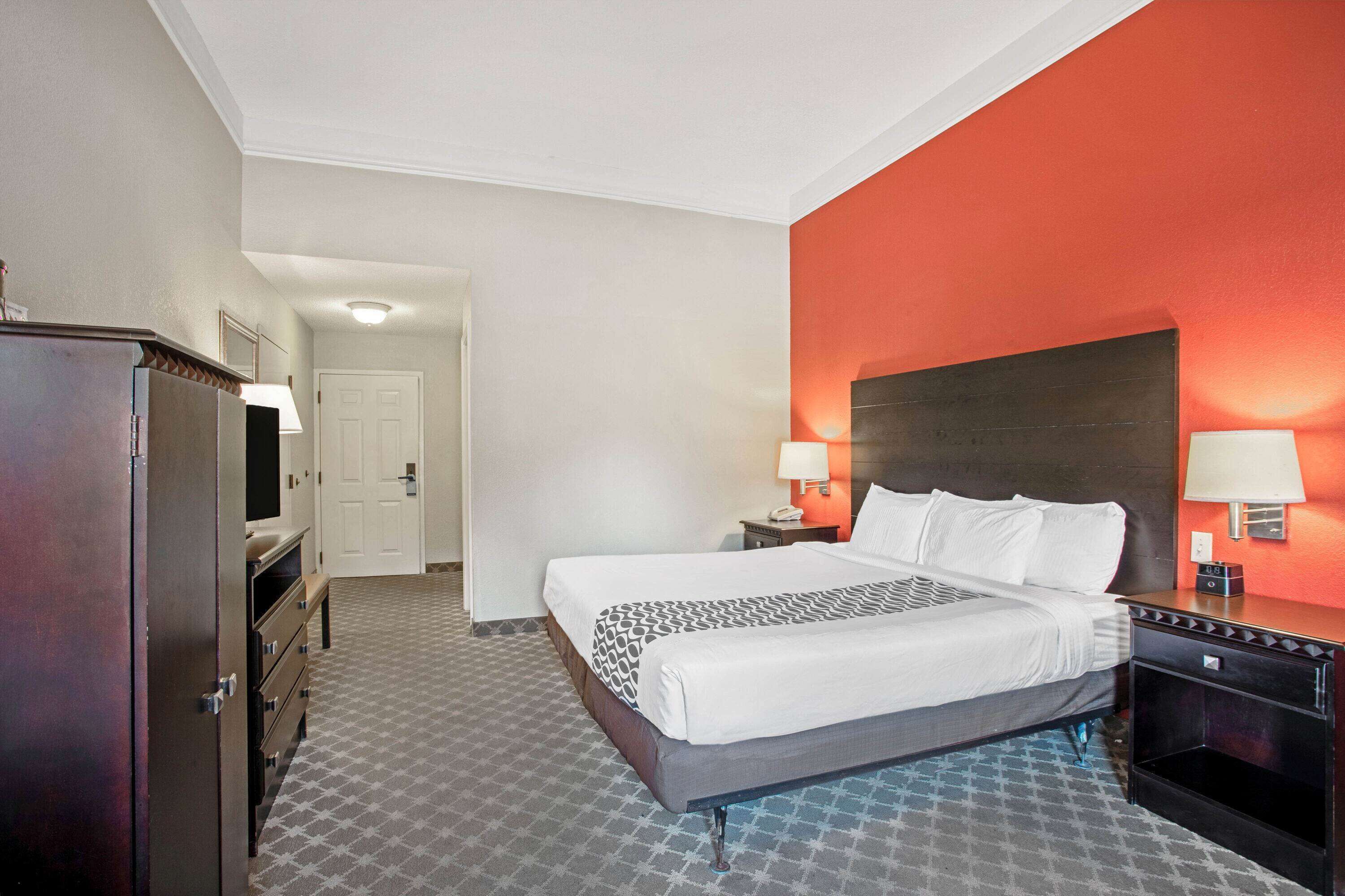 Una habitación de hotel con una cama grande, dos mesitas de noche con lámparas, un armario y un televisor.