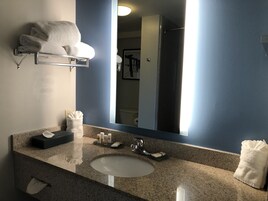 A bathroom with a granite countertop, a white sink, a towel rack with folded towels, a mirror, and toiletries.