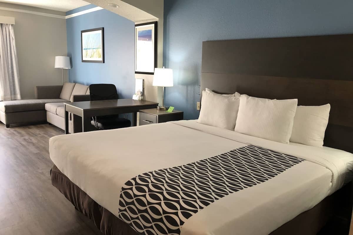 A hotel room with a large bed, a desk, a chair, and a lamp.