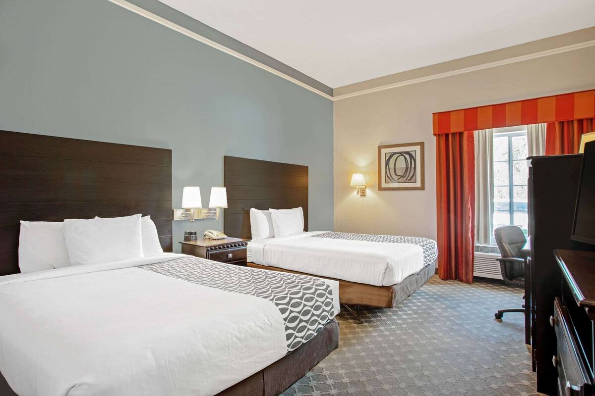 A hotel room with two beds, a desk, a chair, a TV, and a window with curtains.