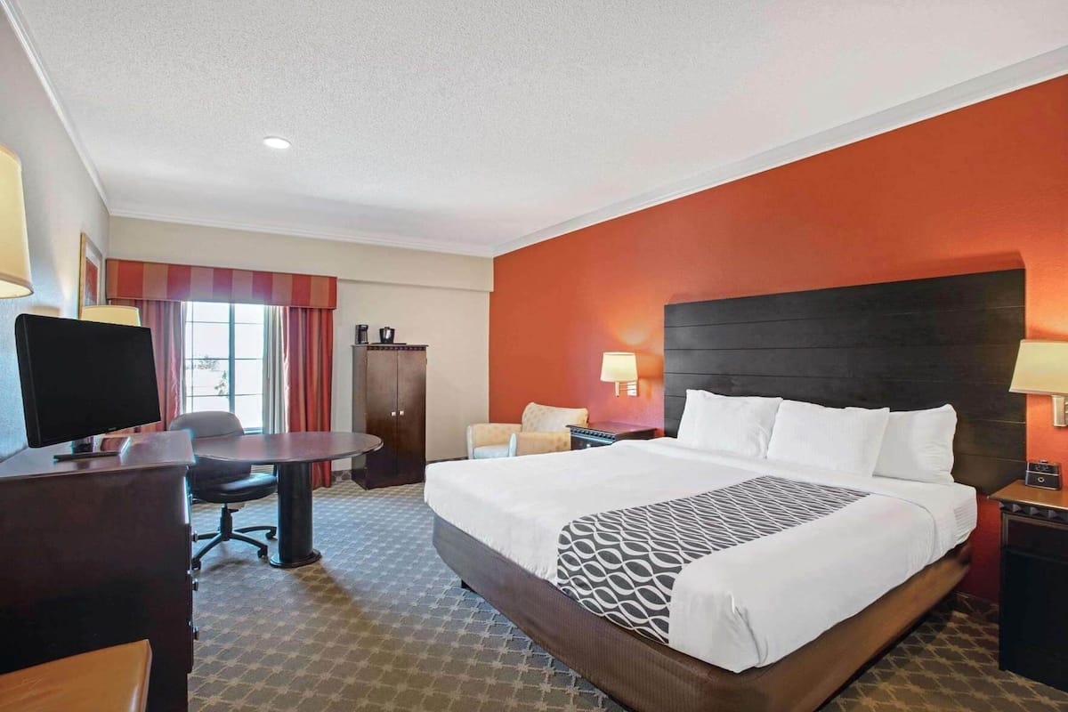 A hotel room with a large bed, a desk, a chair, a TV, and a wardrobe.