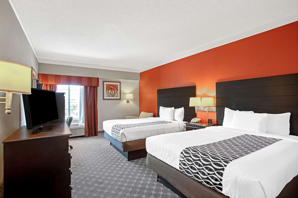 A hotel room with two beds, a TV, a desk, and a window with curtains.