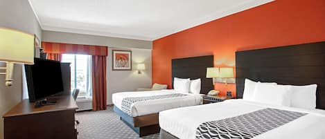 Habitación de hotel con dos camas, televisión, escritorio y ventana con cortinas.