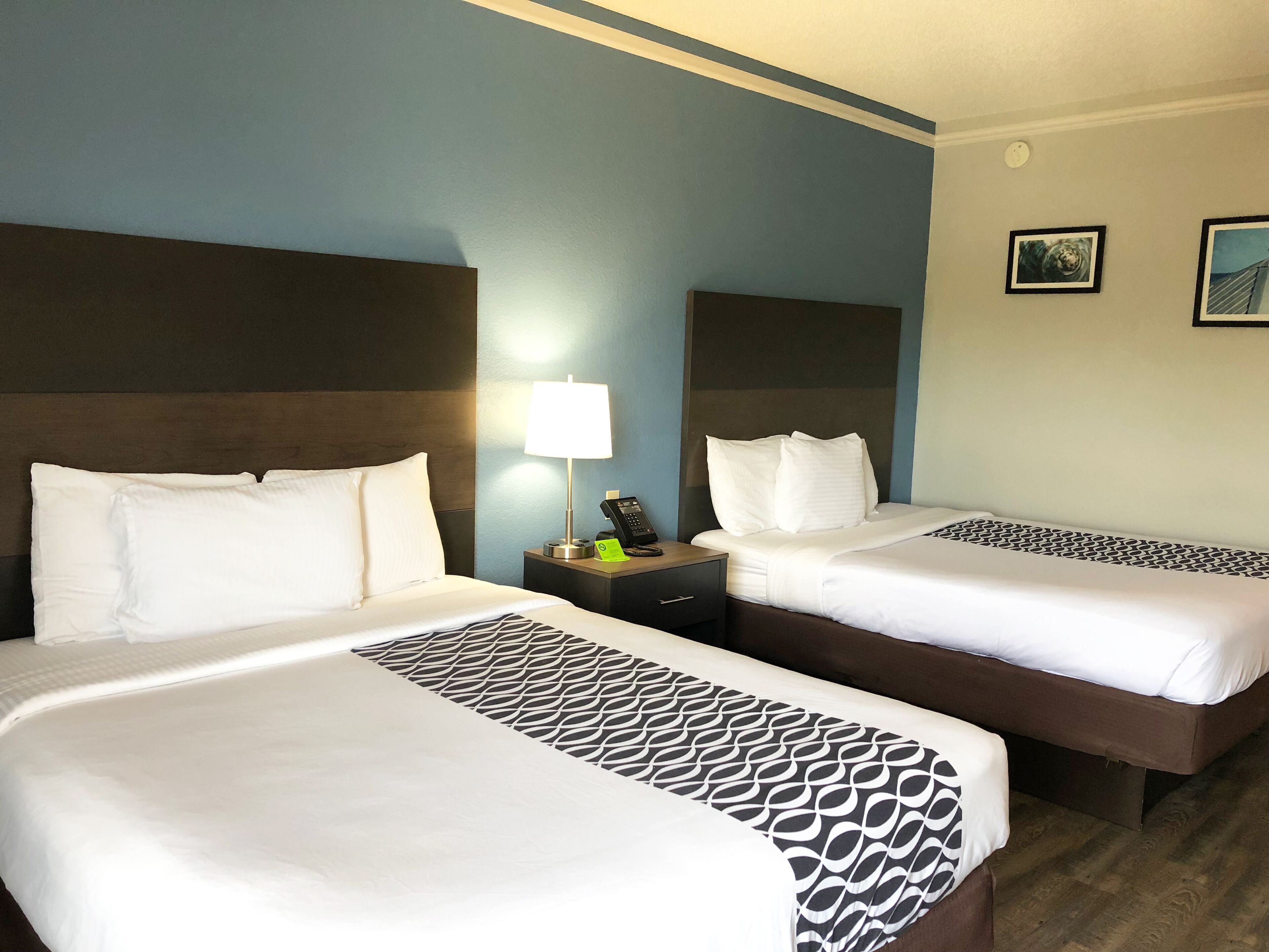 A hotel room with two beds, a nightstand with a lamp, a phone, and a small table with a green item on it.
