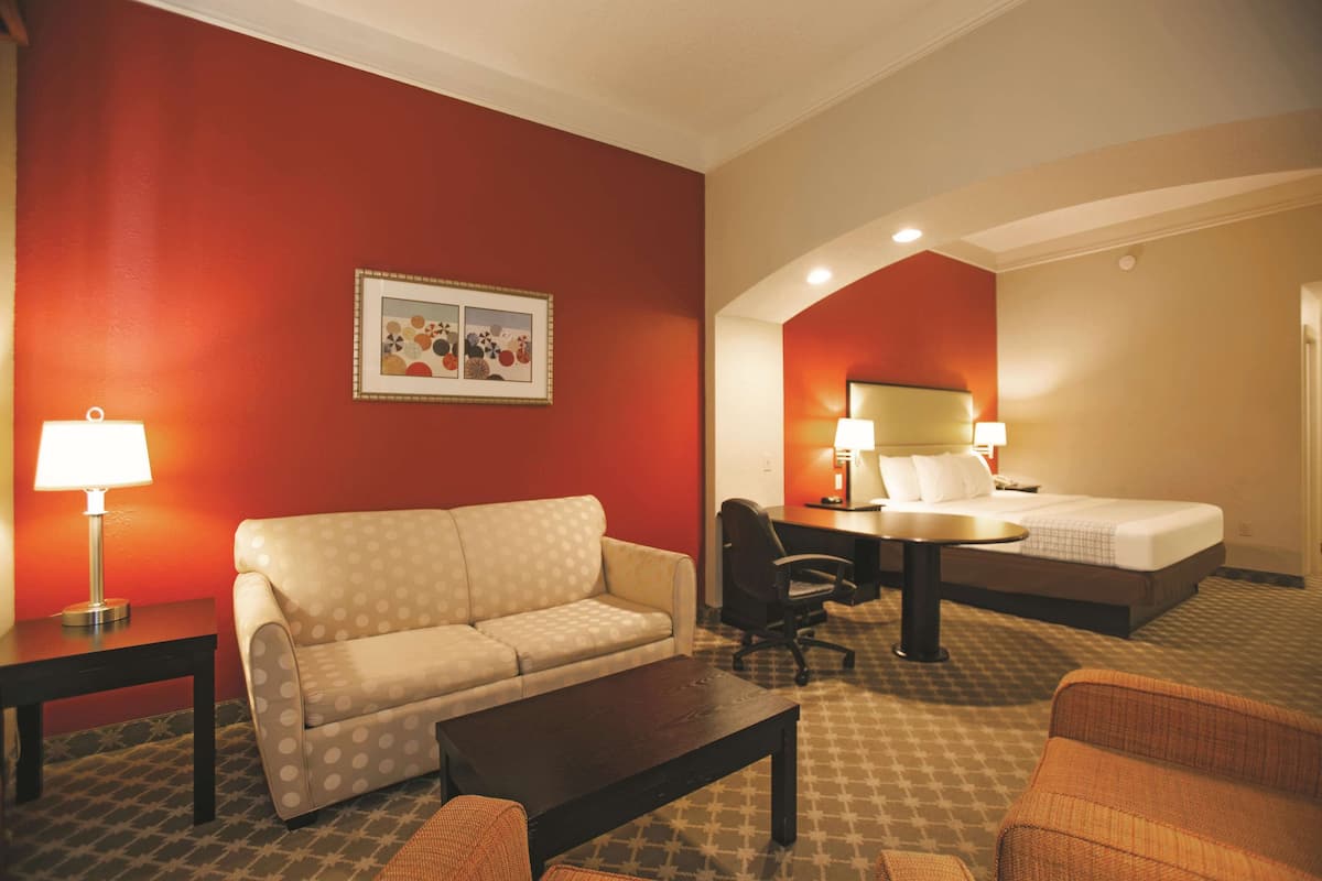 A hotel room with a red wall, a bed, a sofa, a desk, and a chair.