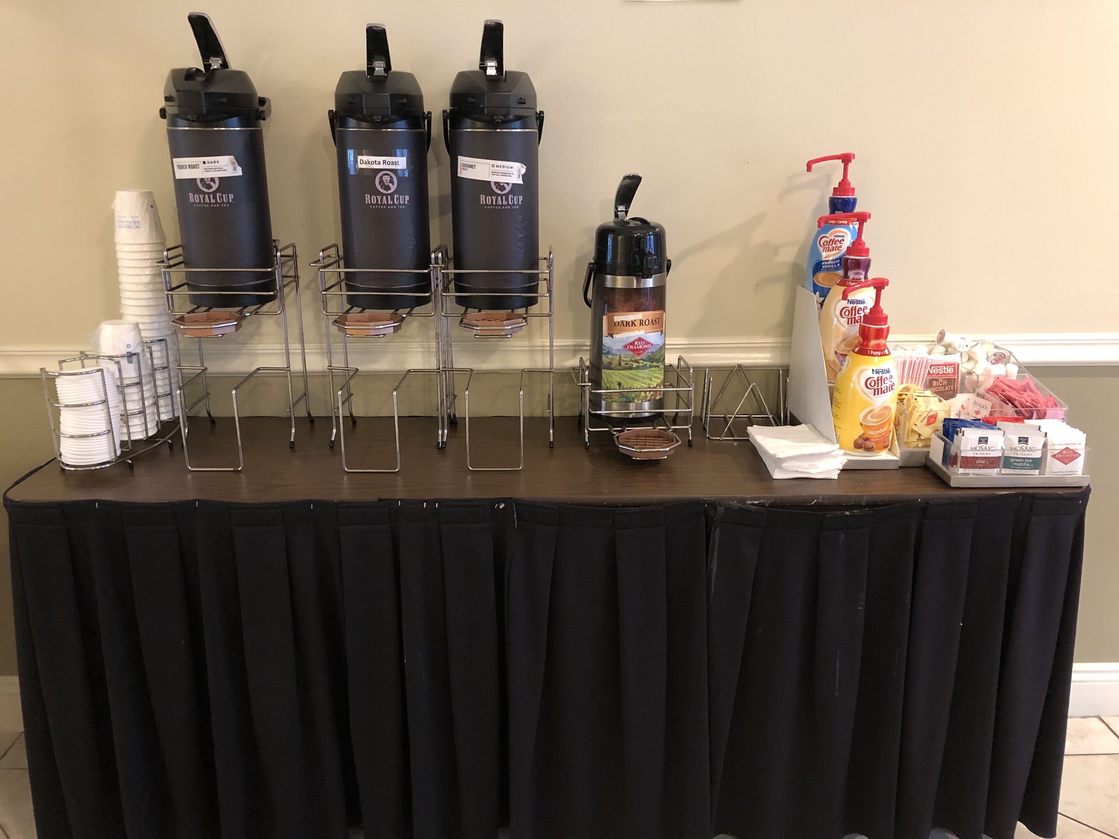 A coffee station with multiple dispensers, disposable cups, and various coffee creamer options.