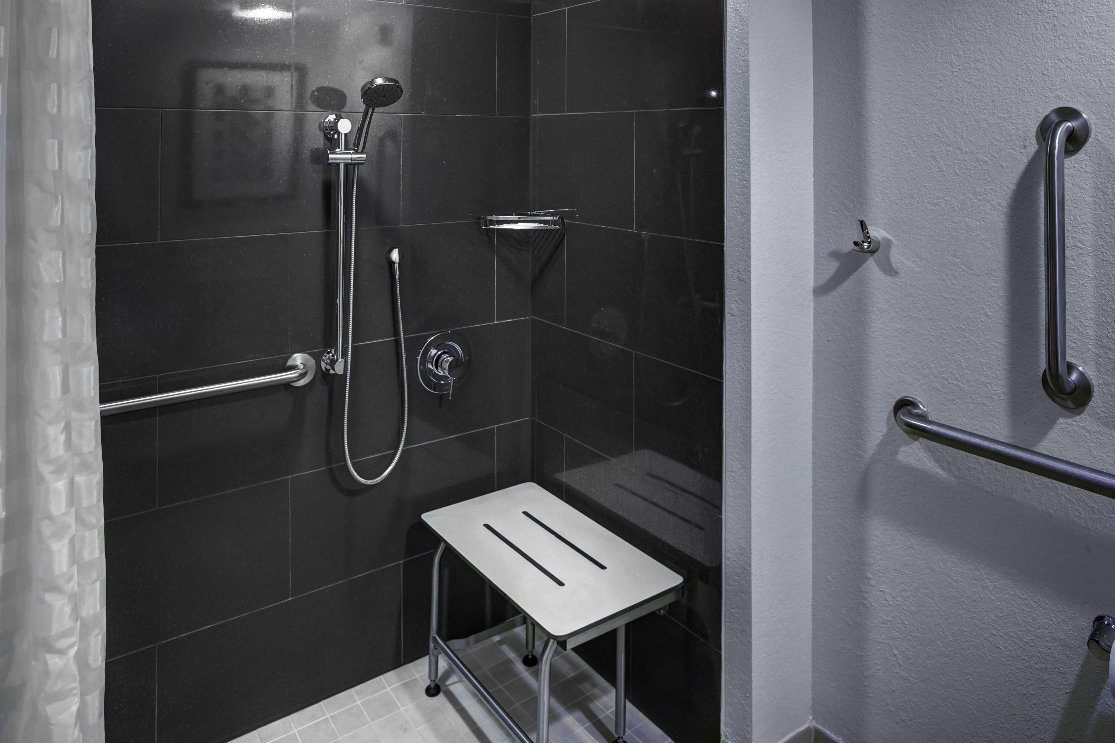 Een kleine, moderne douchehoek met een handdouche, een kraan op de muur en een opstapje voor toegankelijkheid.