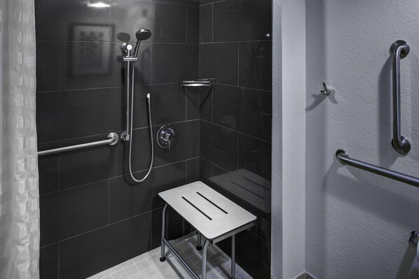 Un pequeño espacio de ducha moderno, con cabezal de ducha de mano, grifo empotrado en la pared y un taburete para facilitar el acceso.