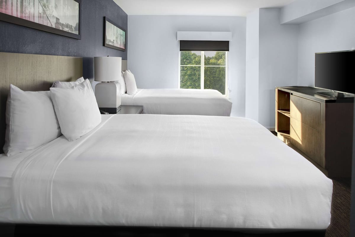 A hotel room with a large bed, a smaller bed, a TV, and a window with a view of trees.