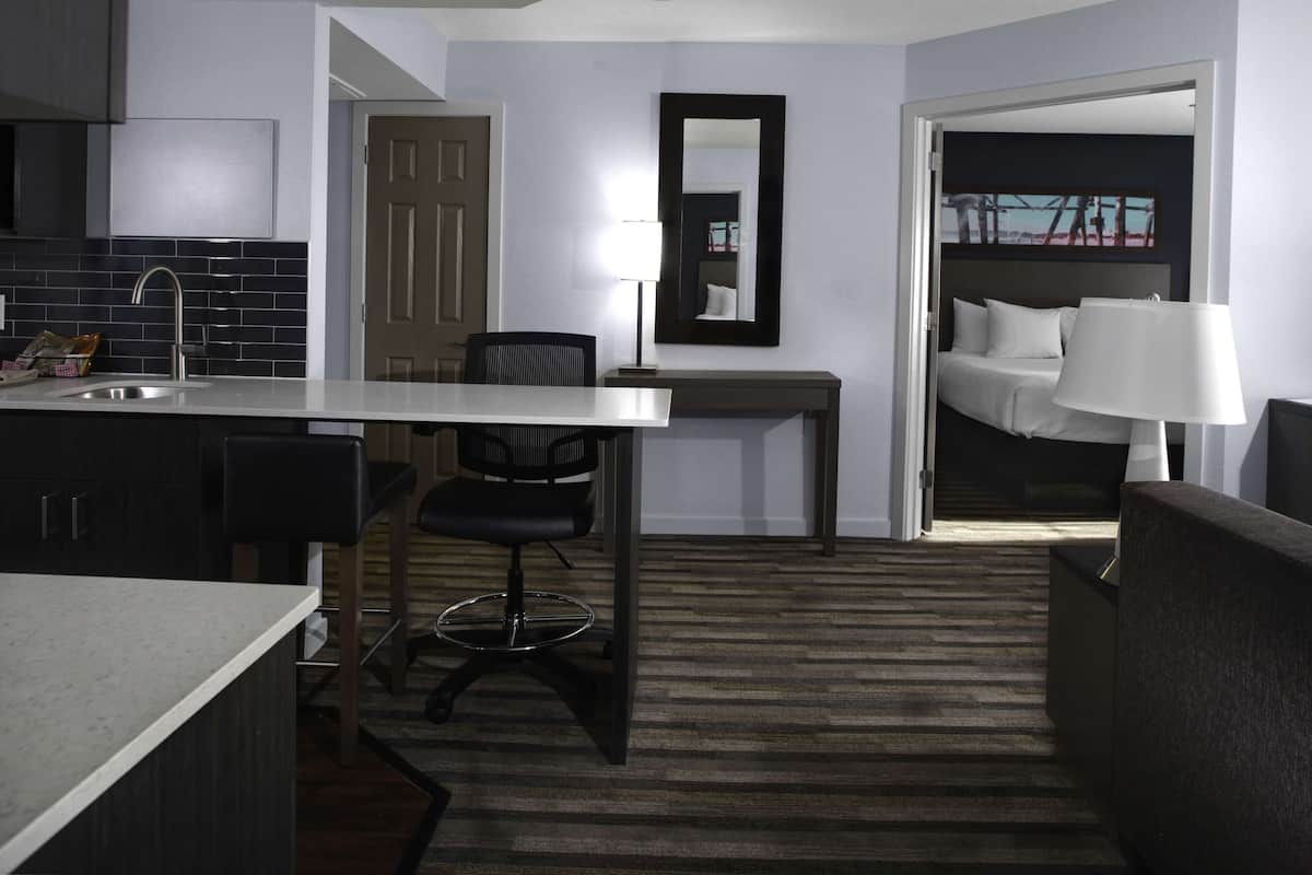 A modern hotel room with a kitchen area, a dining table, a single bed, and a sofa.