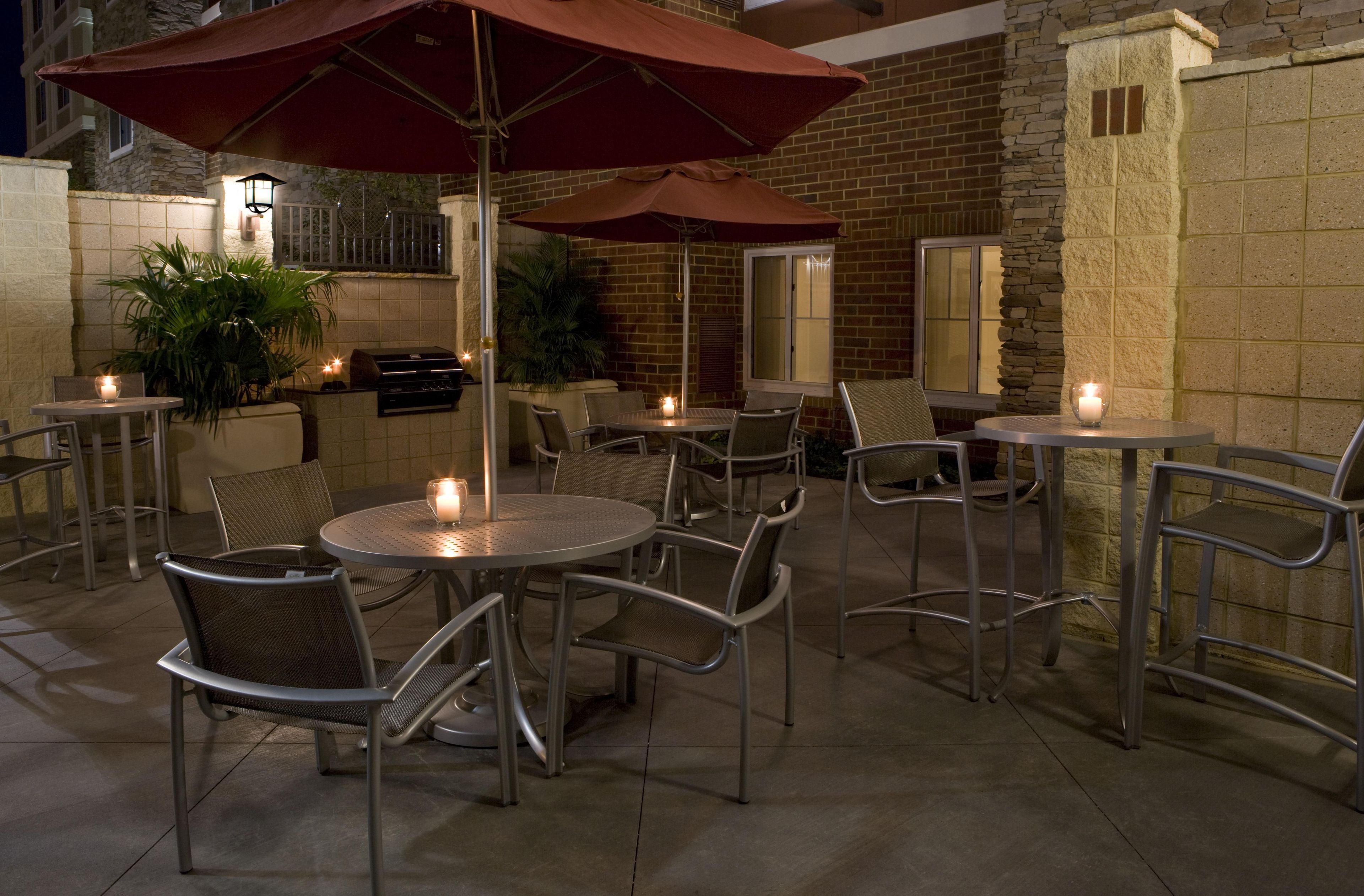 Un espace extérieur aménagé en terrasse, avec des tables et des chaises rondes, des parasols rouges et des bougies.