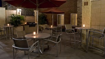 Un espace extérieur aménagé en terrasse, avec des tables et des chaises rondes, des parasols rouges et des bougies.