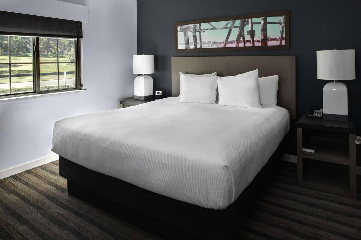 A neatly made bed with white linens, a headboard, and two bedside tables with lamps.