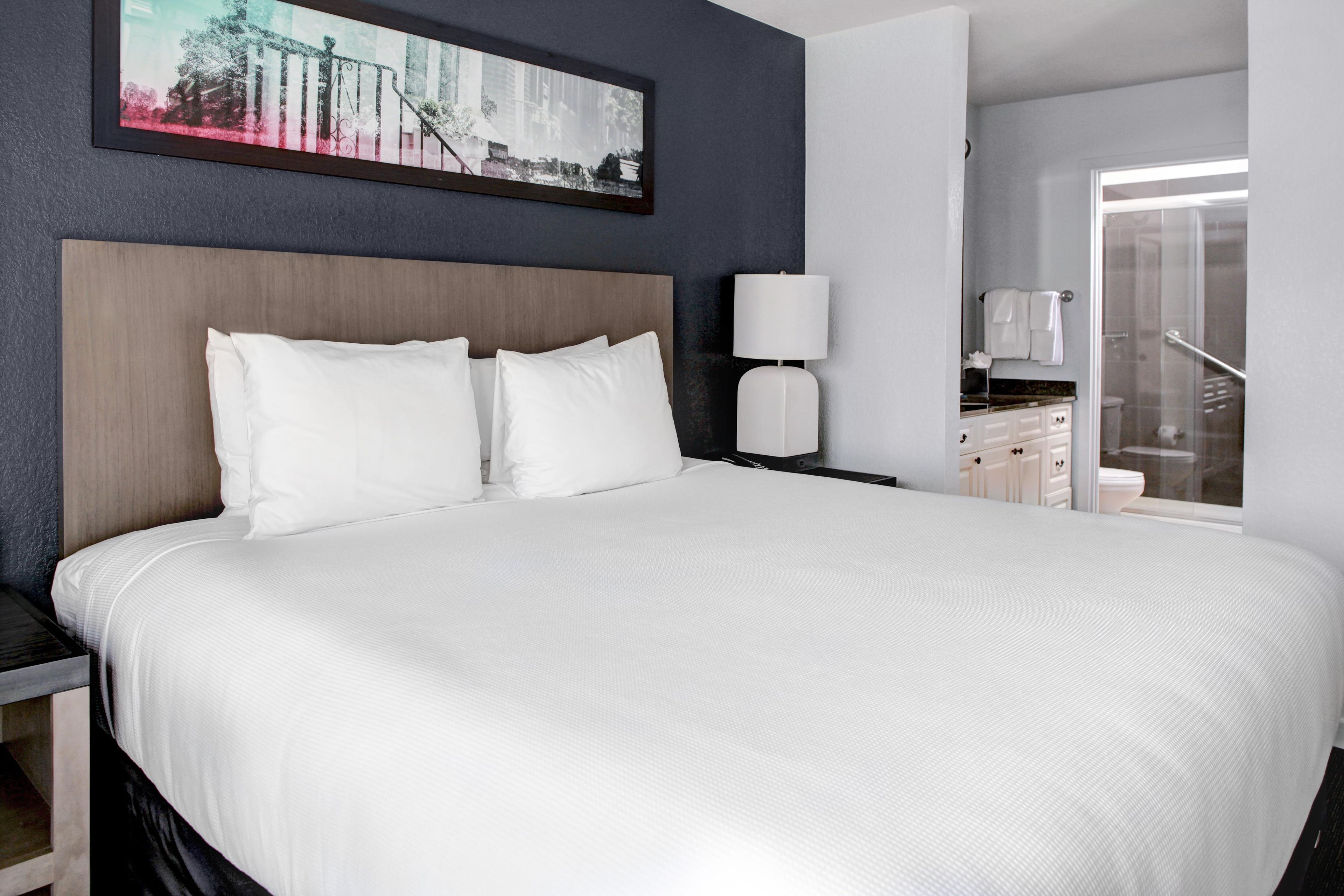 Une chambre d’hôtel avec un grand lit, une table de chevet, une lampe et une salle de bain visible à travers une porte ouverte.
