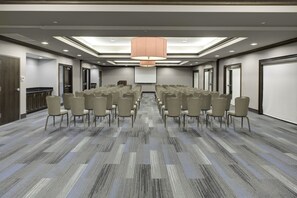 Un salón de conferencias con filas de sillas, una pantalla grande y una lámpara en el techo.