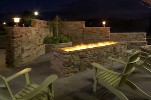 Un patio exterior con una chimenea de piedra y sillones Adirondack verdes.