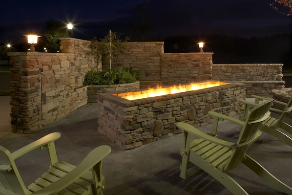 Un patio exterior con una chimenea de piedra y sillones Adirondack verdes.