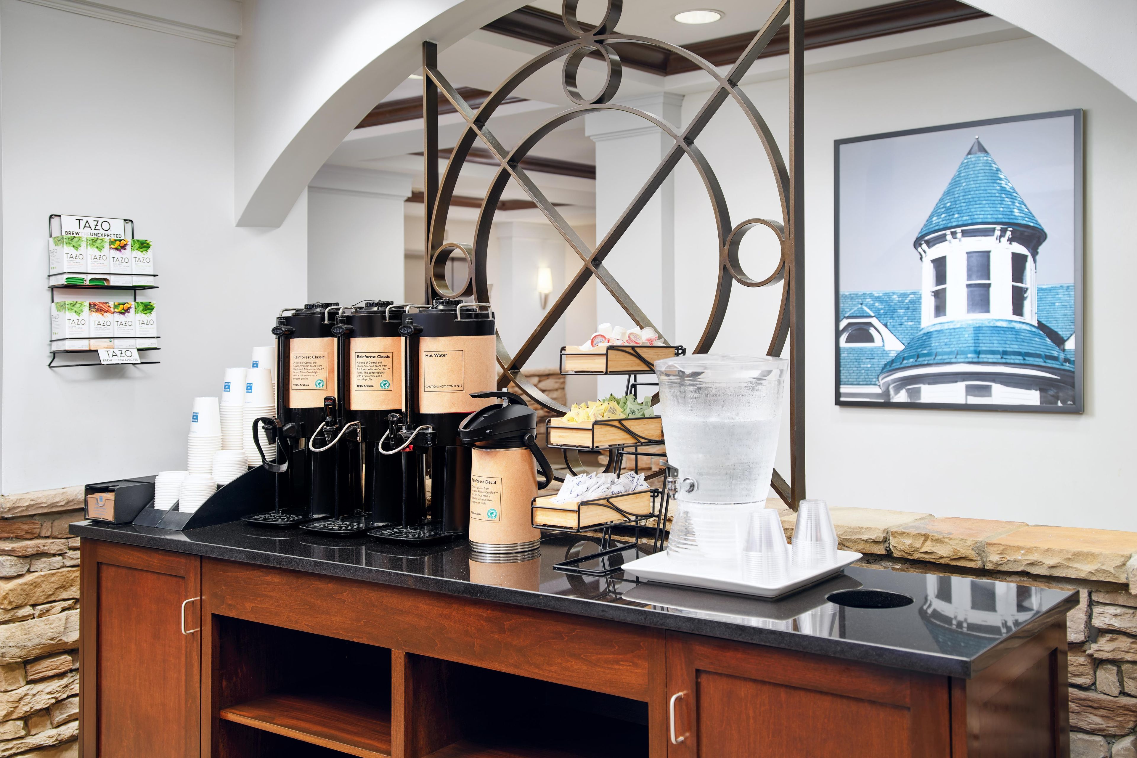 A coffee station with multiple brewing options, a water dispenser, and a framed picture of a building on the wall.