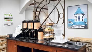 A coffee station with multiple brewing options, a water dispenser, and a framed picture of a building on the wall.