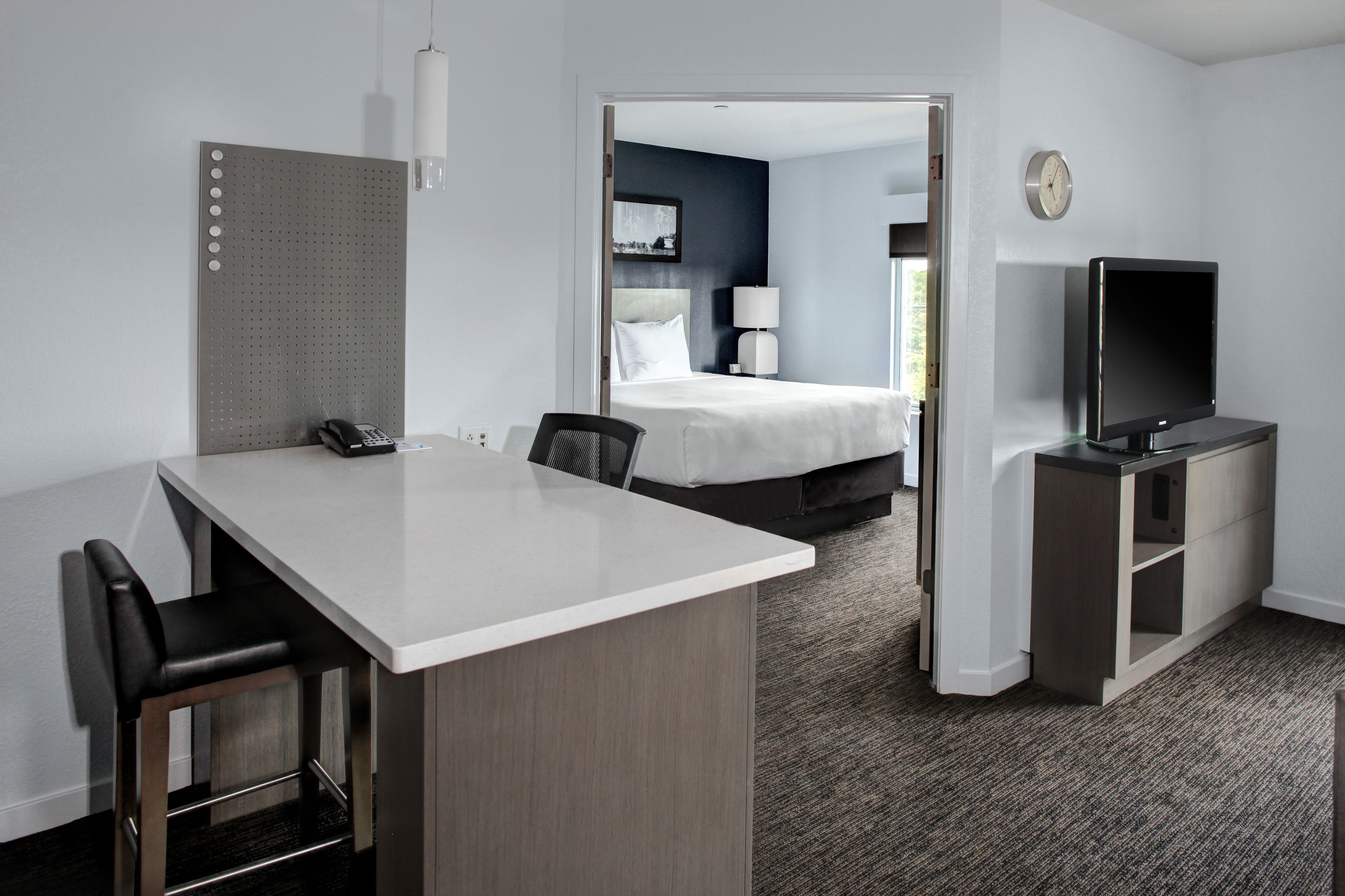A hotel room with a desk, chairs, a bed, a TV, and a door leading to another room.